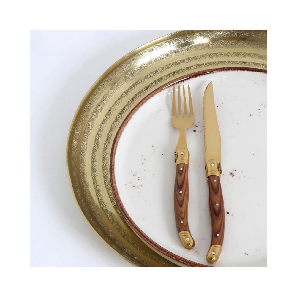 Ένα μαχαίρι για μπριζόλες σε χρυσό χρώμα και ρουστίκ λαβή στο χρώμα του ξύλου τοποθετημένο σε λευκόχρυσο πιάτο