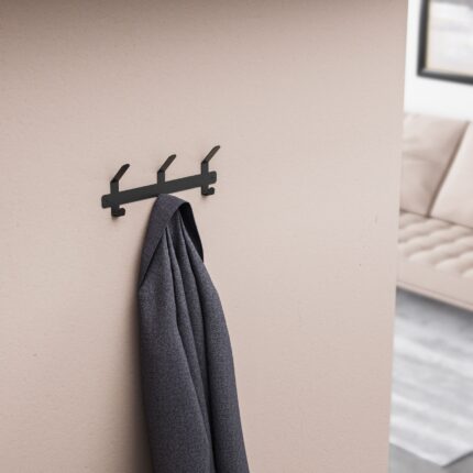 Μεταλλική μαύρη κρεμάστρα 3 θέσεων τοποθετημένη σε μπεζ τοίχο με κρεμασμένο ένα γκρι παλτό