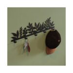 Μία διακοσμητική μαύρη μεταλλική κρεμάστρα σε χακί τοίχο με κρεμασμένο ένα καπέλο και κλειδιά