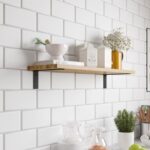 Ένα ξύλινο ράφι που στηρίζεται με μαύρες μεταλλικές γωνίες σε λευκό τοίχο