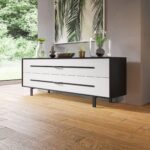 Ένας μπουφές σαλονιού με λευκά συρτάρια και μαύρα μεταλλικά πόδια επίπλων, τοποθετημένο επάνω σε ξύλινο δάπεδο σαλονιού