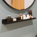 Ένα μαύρο μεταλλικό τετραγωνισμένο ράφι σε πράσινο τοίχο με μαύρο μεταλλικό καθρέπτη από πάνω