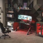 Ένα γκρι δωμάτιο με βιβλιοθήκη και με ένα μεταλλικό γραφείο gaming με δύο οθόνες